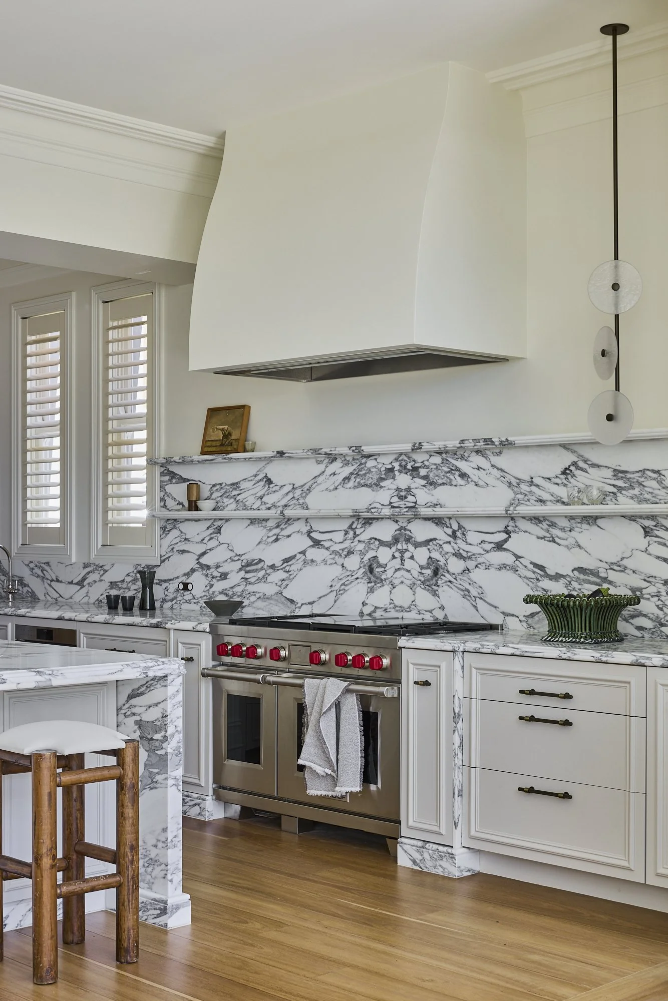 Modern kitchen with white cabinetry, marble countertops and backsplash, stainless steel stove, and wooden flooring.