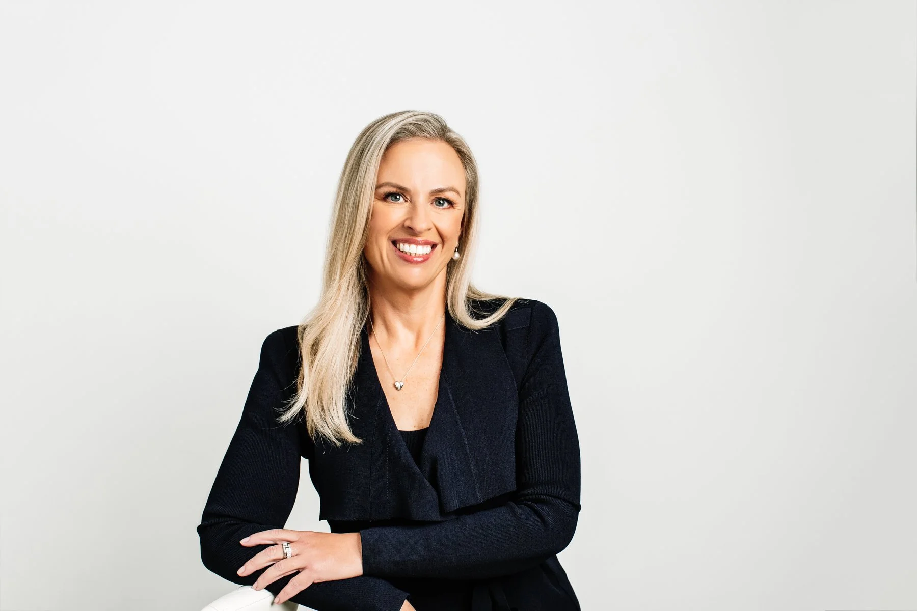 Professional headshot of a smiling blonde businesswoman wearing a black jacket, photographed against a clean white studio background in Sydney.