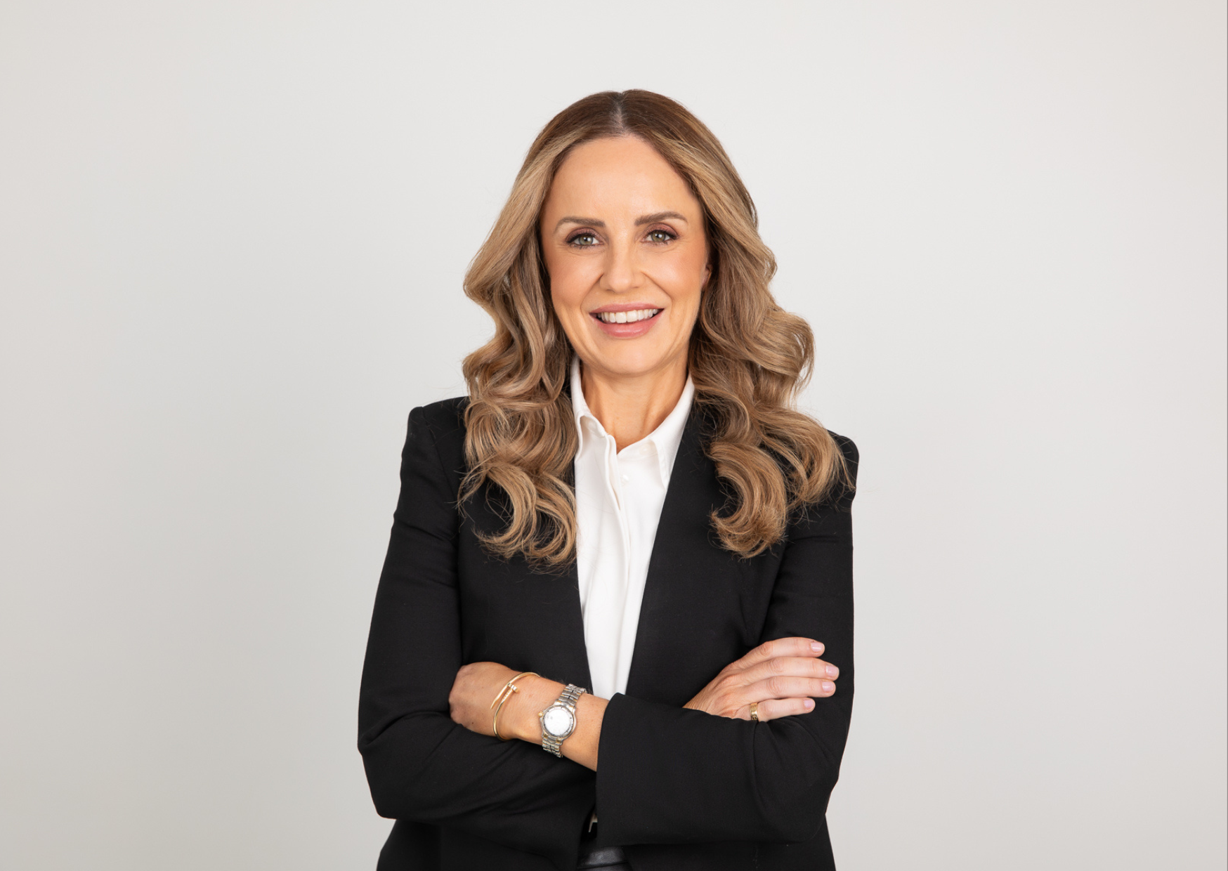 Natural LinkedIn headshot of a smiling professional woman in a black blazer and white shirt, photographed in a Sydney studio.