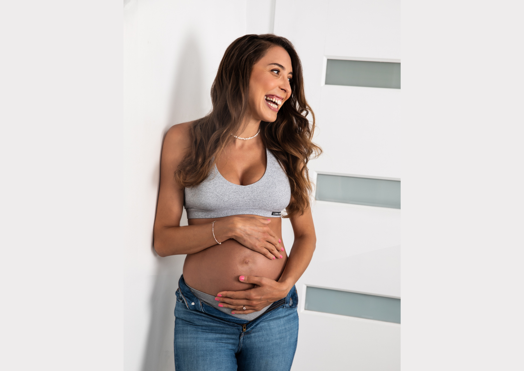 Joyful maternity portrait of a laughing pregnant woman cradling her bump — maternity photography by Simona Janek