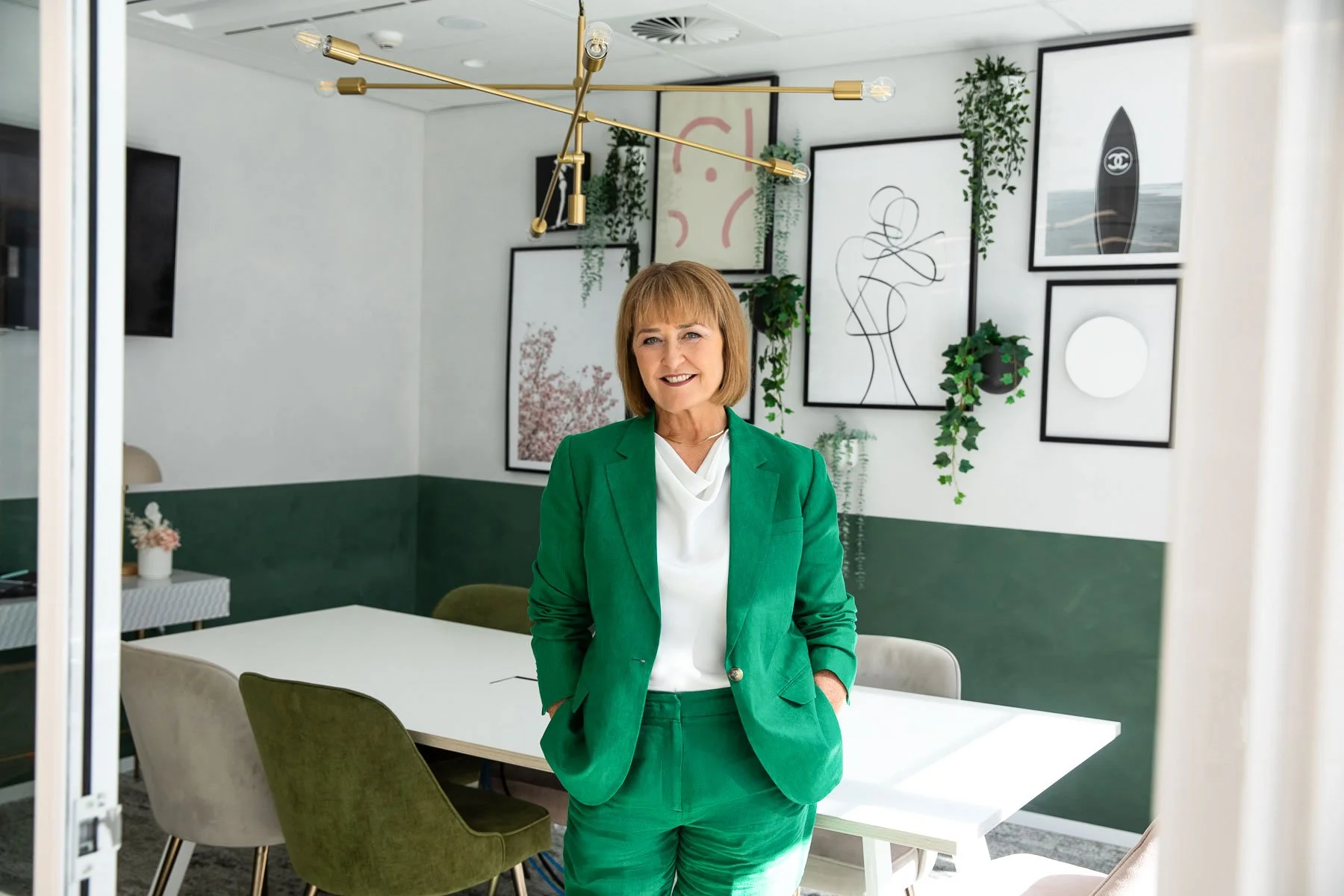 Personal branding photography session featuring a professional woman in a green suit standing in a modern office space, showcasing a confident and approachable business brand image.