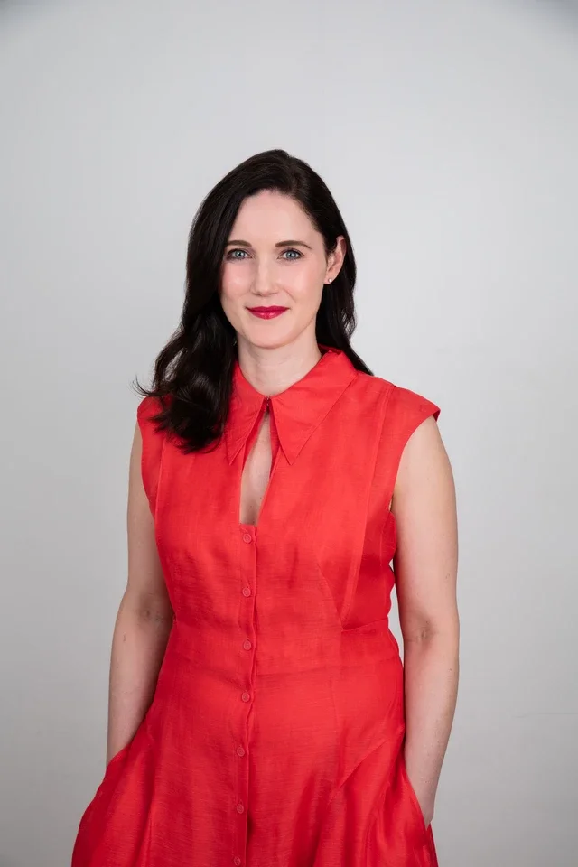Professional hair and makeup in-studio service featuring a woman in a red dress with polished makeup and styled hair, photographed against a clean studio background.