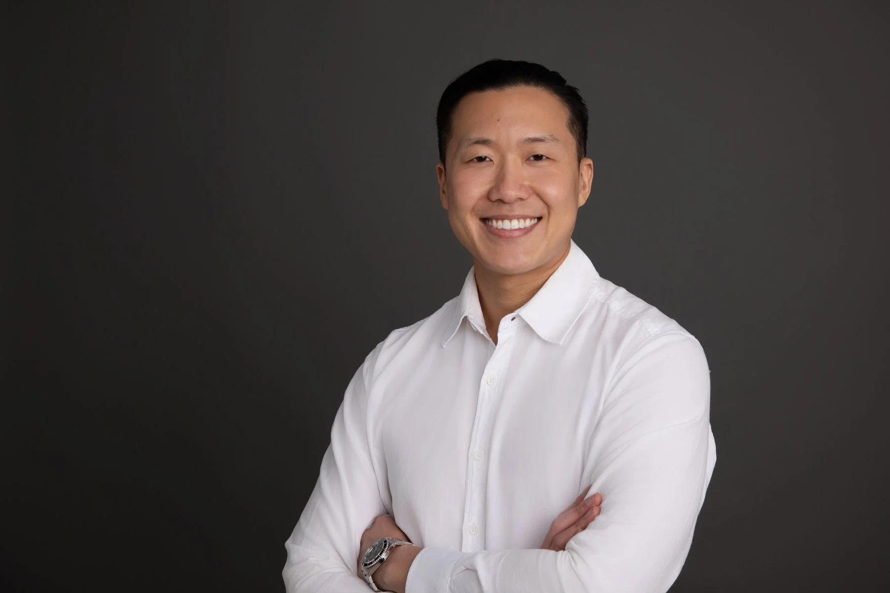 Alt text: Professional headshot of a smiling business man in a white shirt, photographed against a dark studio background in Sydney.