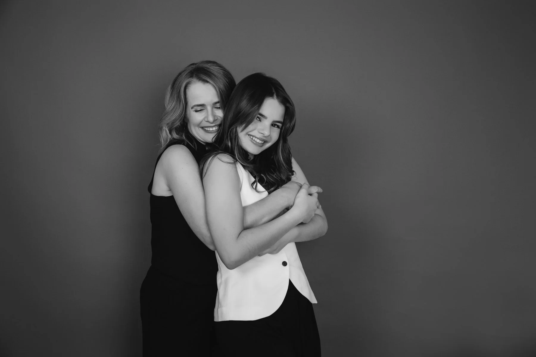 Black and white studio portrait of a mother and teenage daughter hugging and laughing together