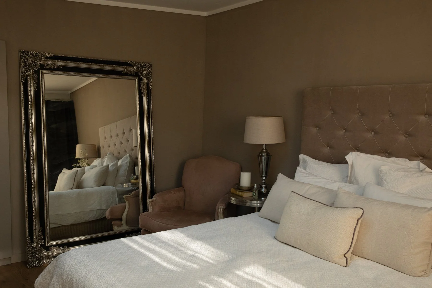 Elegant boudoir photography studio bedroom with tufted headboard, ornate floor mirror, and warm neutral tones