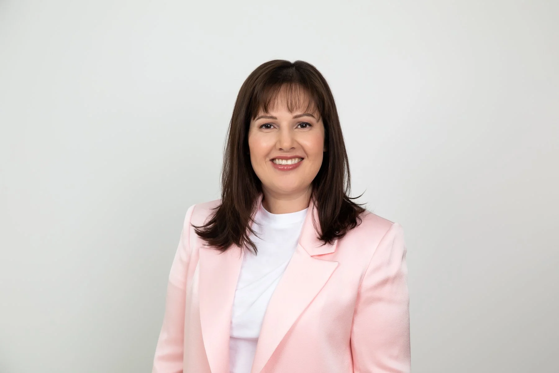 Professional headshot of a smiling woman wearing a pink blazer and white top against a clean studio background in Sydney.