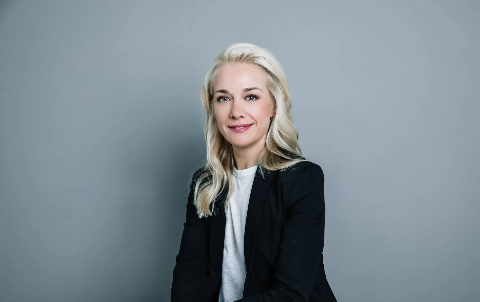 Professional headshot of a woman in a black blazer smiling against a grey background