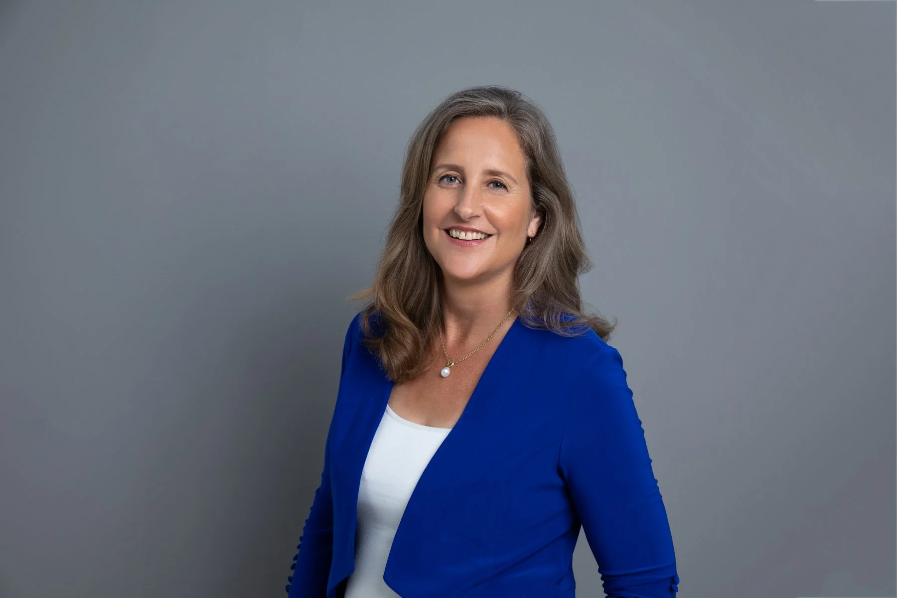 Professional headshot of a smiling woman wearing a blue blazer, photographed against a neutral studio background in Sydney.