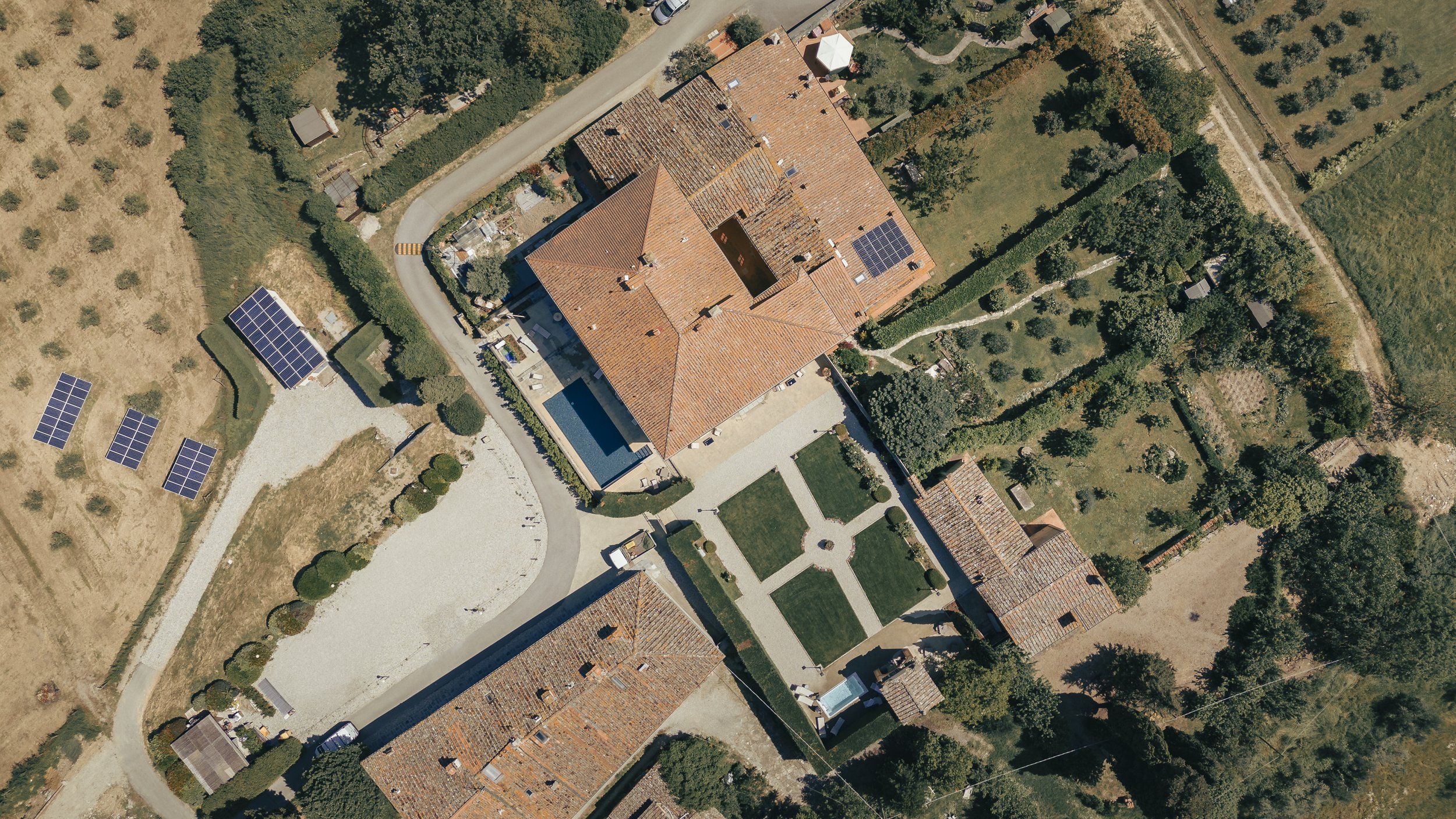 Vista aerea di una grande proprietà con case, piscina, giardini e pannelli solari sui tetti.