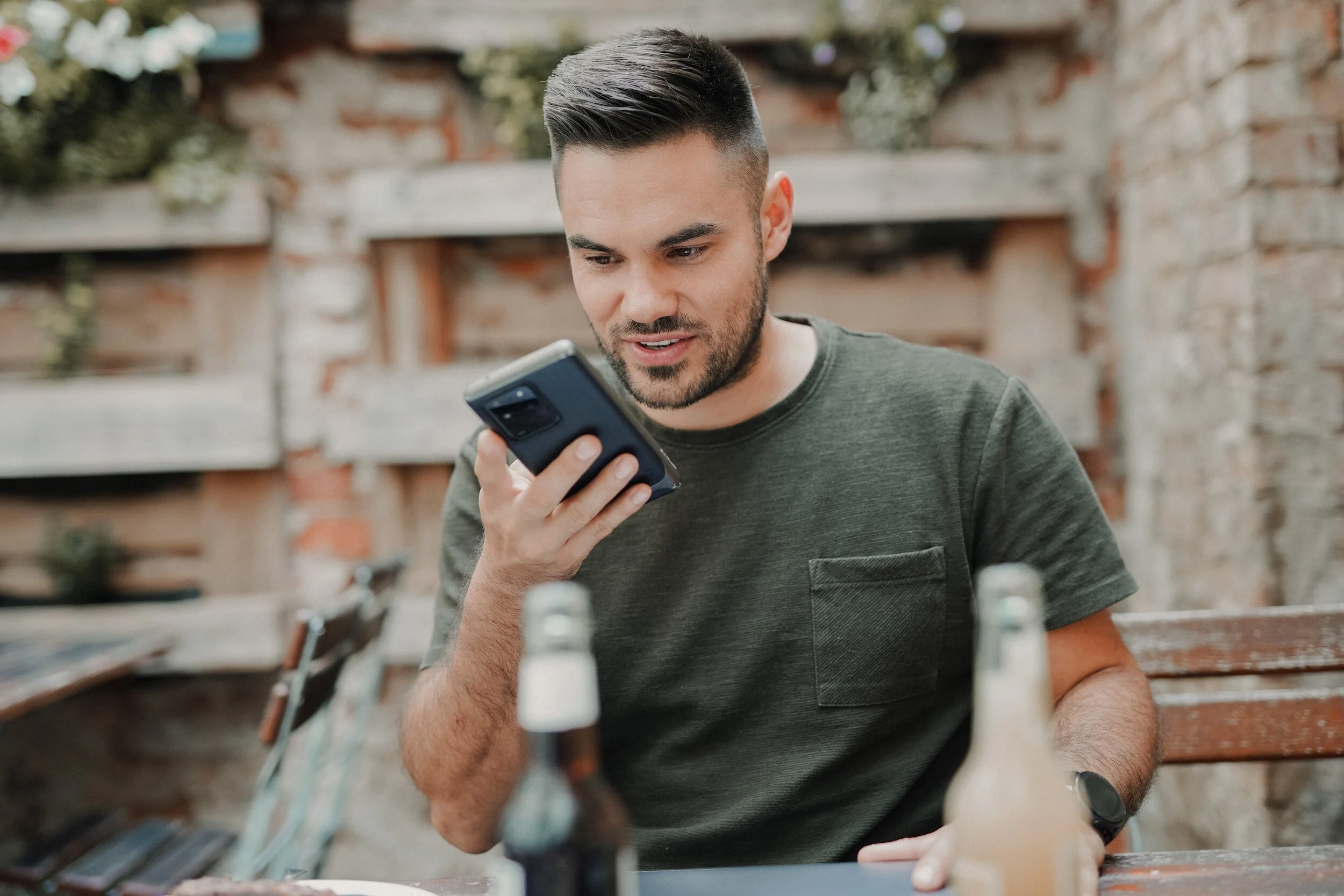 Man sitting outdoors using smartphone with two bottles on the table