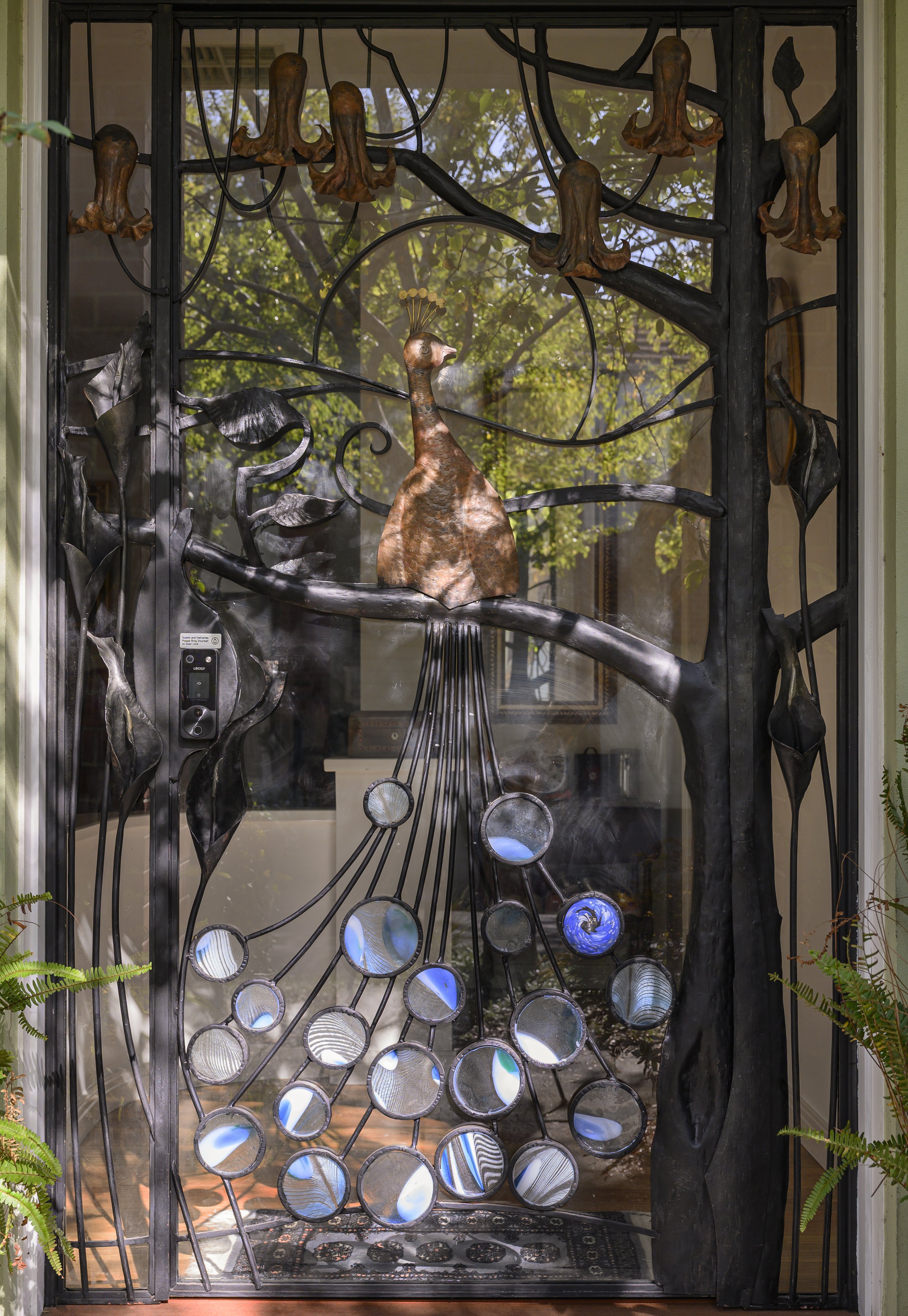 Peacock security door by artist blacksmith David Wood, handmade with forged branches, copper peacock and circular glass tail details.