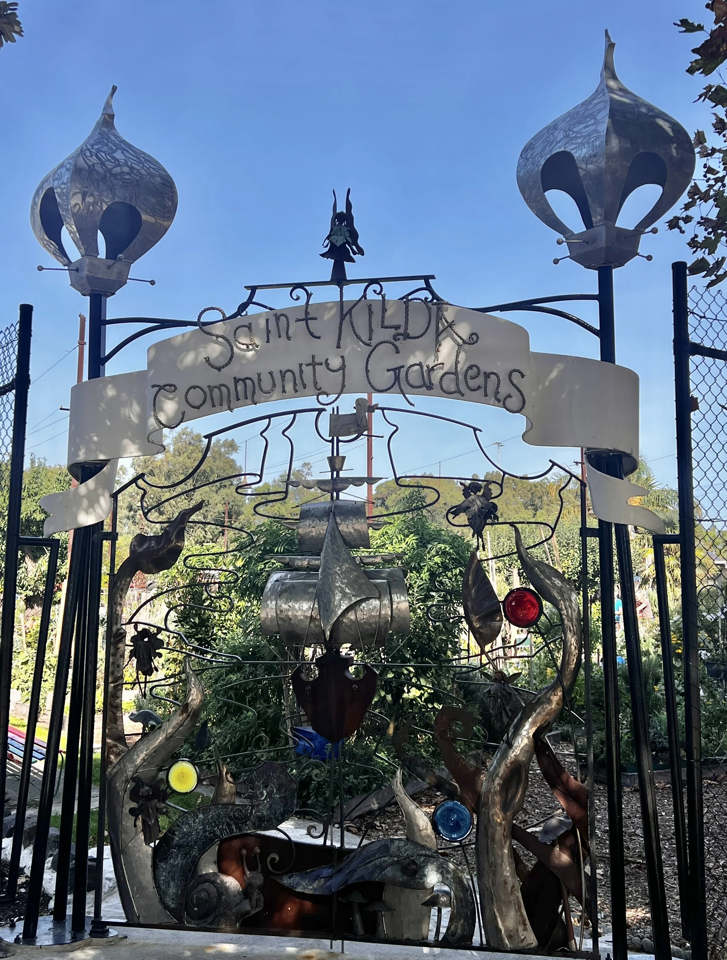 Veg Out Community Garden 25th Anniversary Gate by David Wood of Bent Metal, with ship forms, fairy figures and coloured glass.