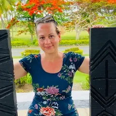 Woman in a blue top with sunglasses on top of her head with a smile.