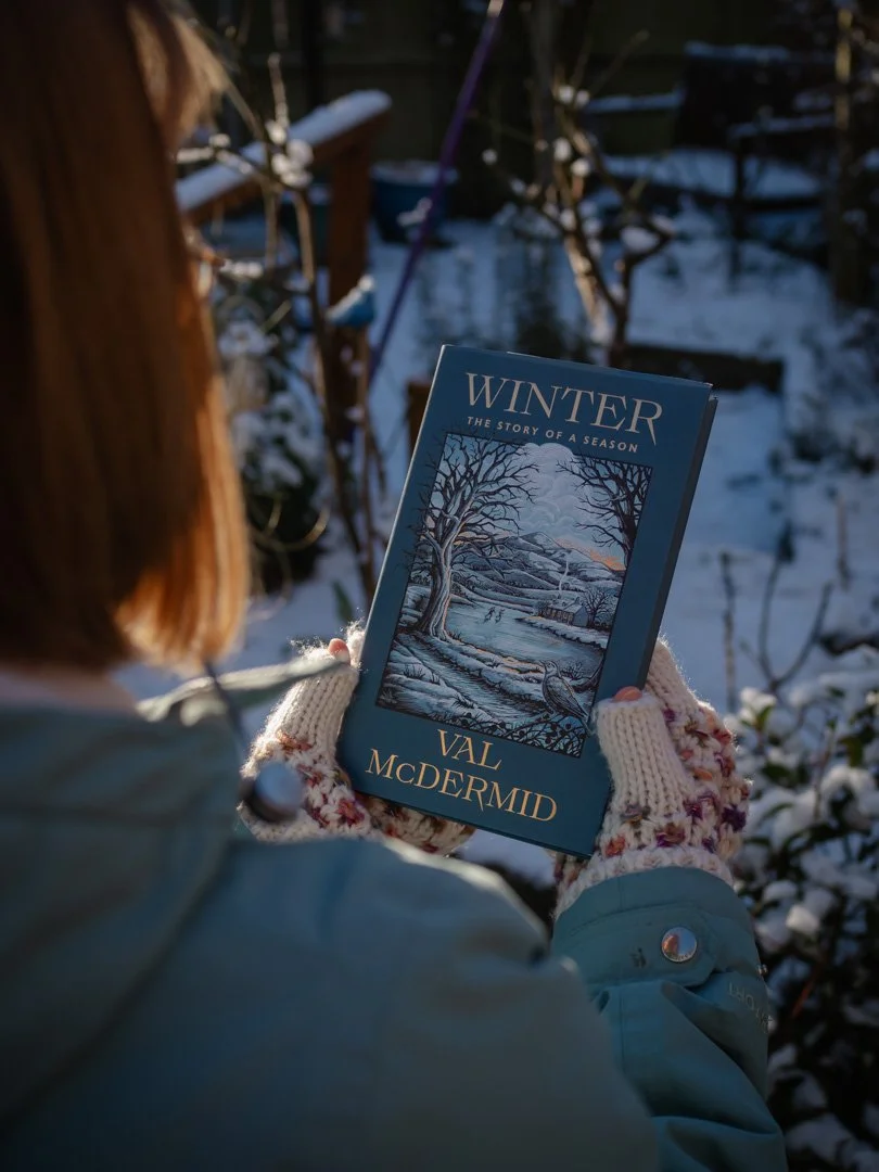 Cover of Winter by Val McDermid held in gloved hands outdoors in a snowy garden