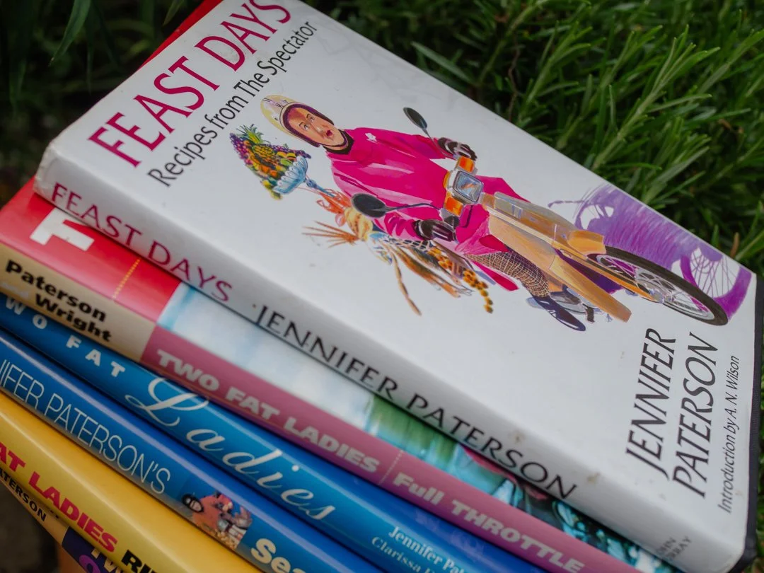 Jennifer Paterson's Feast Days cookbook resting on top of a collection of Two Fat Ladies cookbooks.