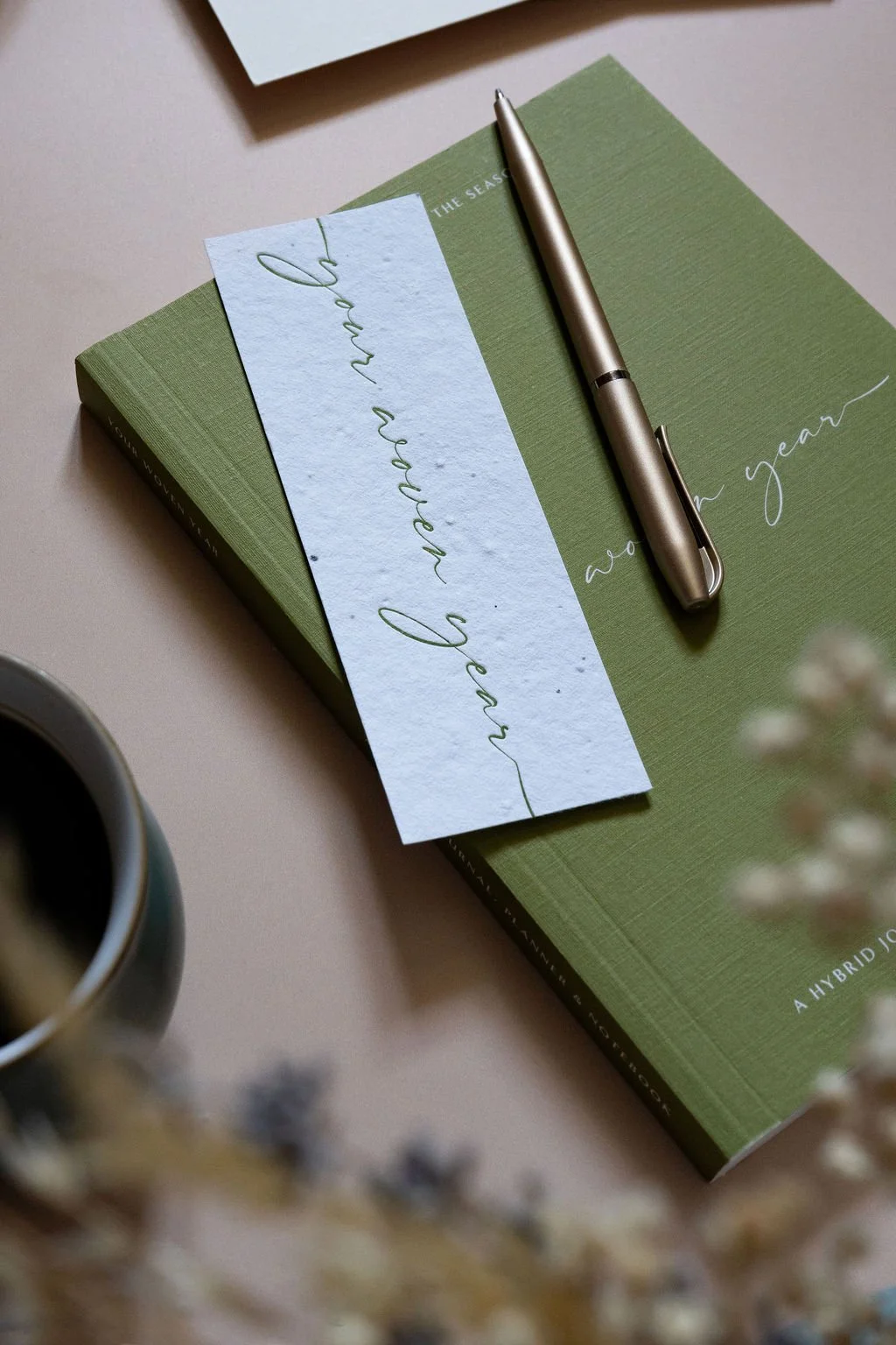 A closed copy of The Woven Year resting on a desk with a pen, symbolising intentional planning and seasonal working.