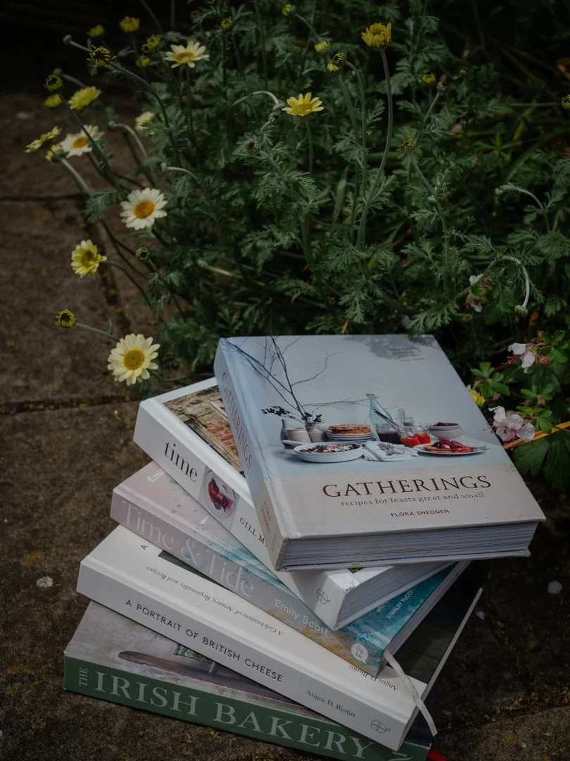 Seasonal cookbooks by contemporary food writers arranged in a stack, celebrating storytelling, memory, and slow seasonal living.