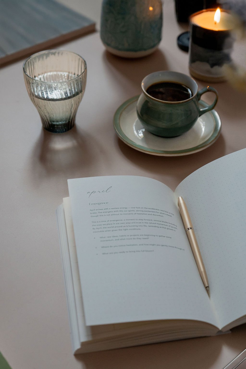 A planner on a desk beside a lit candle, coffee and water, creating a calm space for reflective, seasonal working.