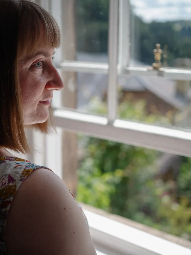 Clementine Rose standing by a window with sunlight on her face, embracing calm and presence