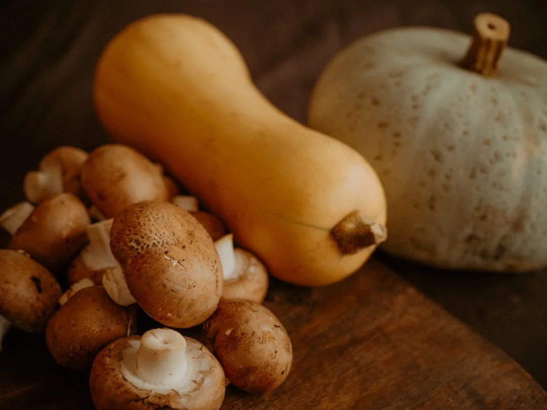 A pile of fresh chestnut mushrooms alongside a butternut squash and a Crown Prince squash, seasonal ingredients for autumn soup recipes.