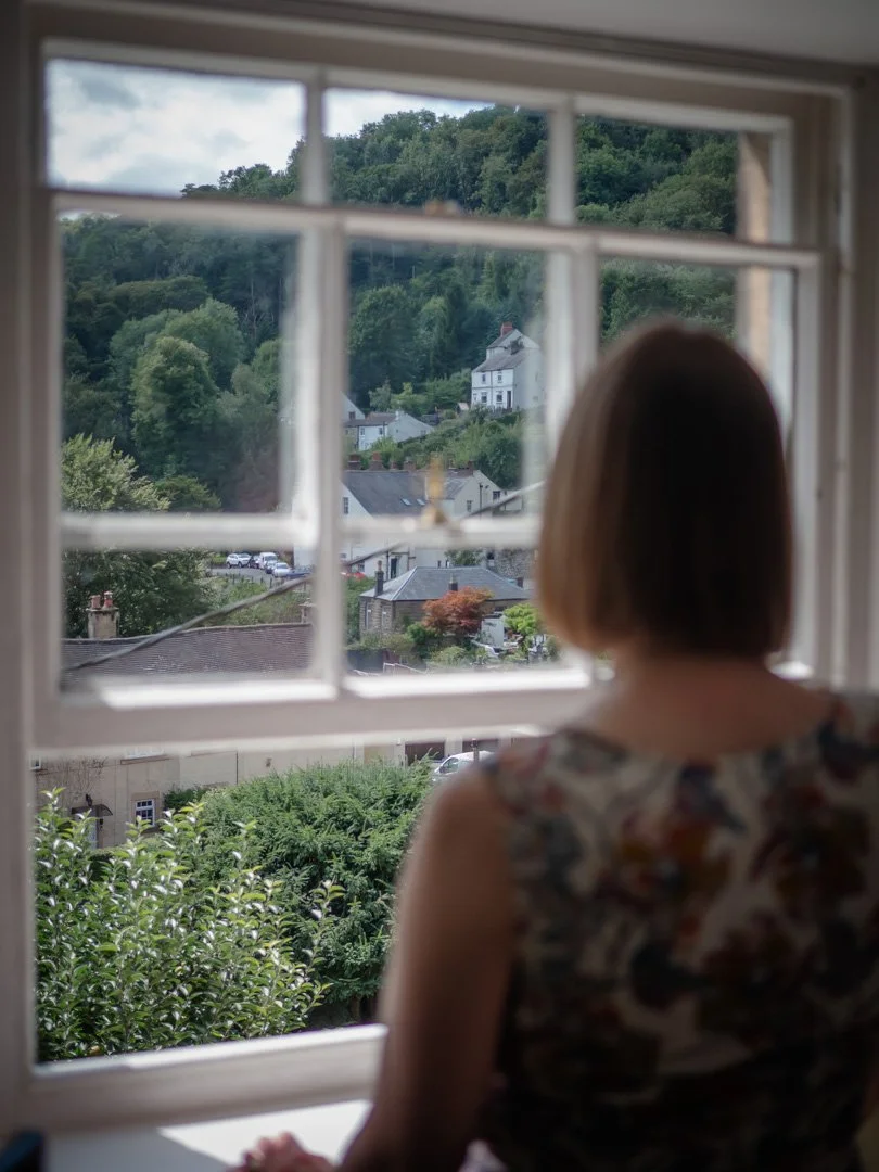 Clementine Rose looking out of an open window toward distant hills, connected to nature and stillness