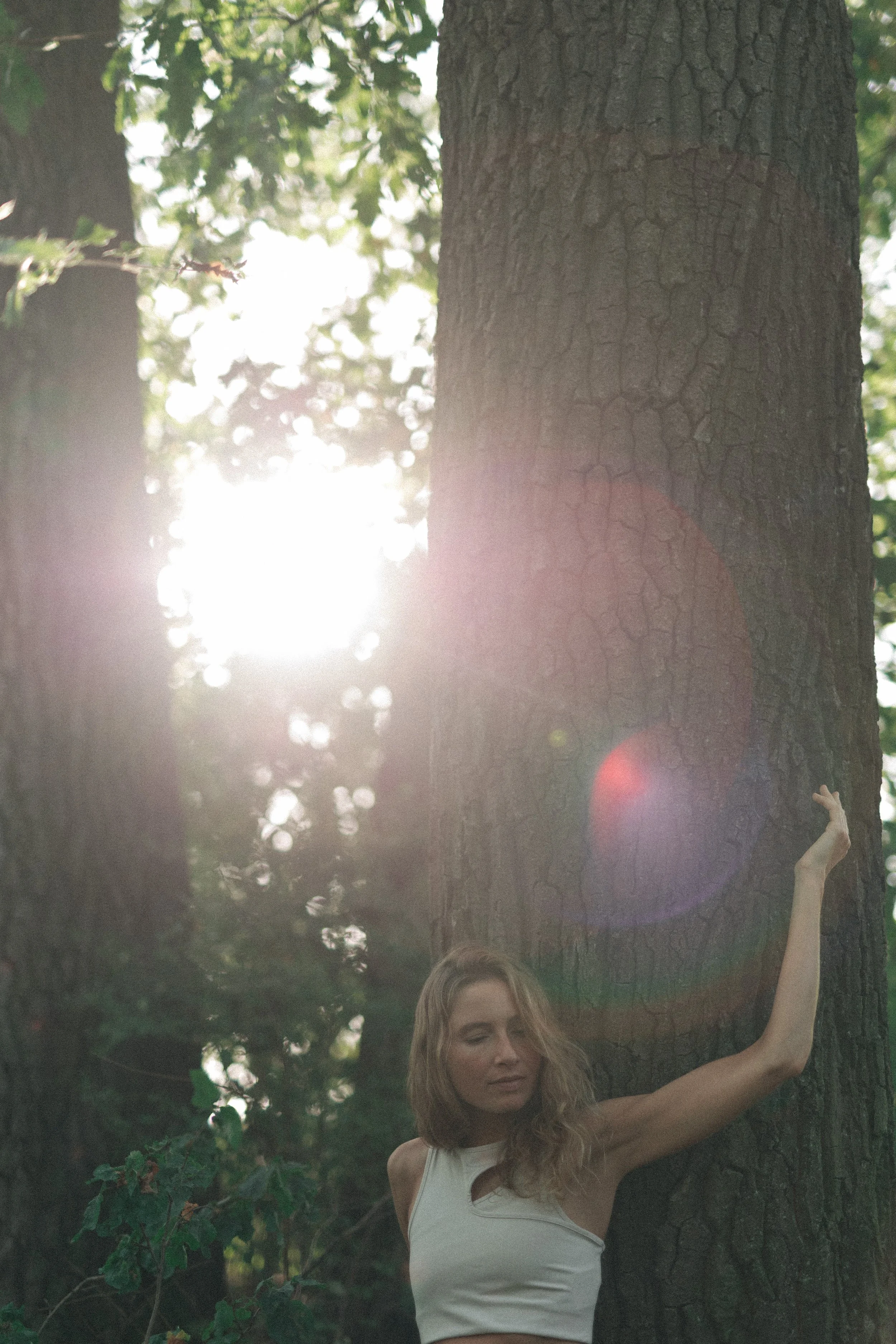 Verena Borell leaning peacefully against a tree beneath woodland branches in Austria.