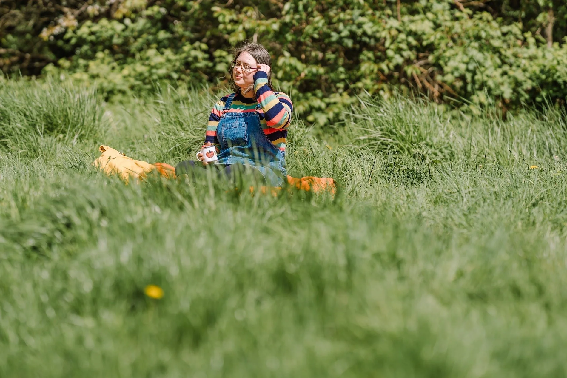 Rhiannon Adler sitting in a sunny grassy field holding a mug, embracing a slower, simpler and more seasonal way of living.
