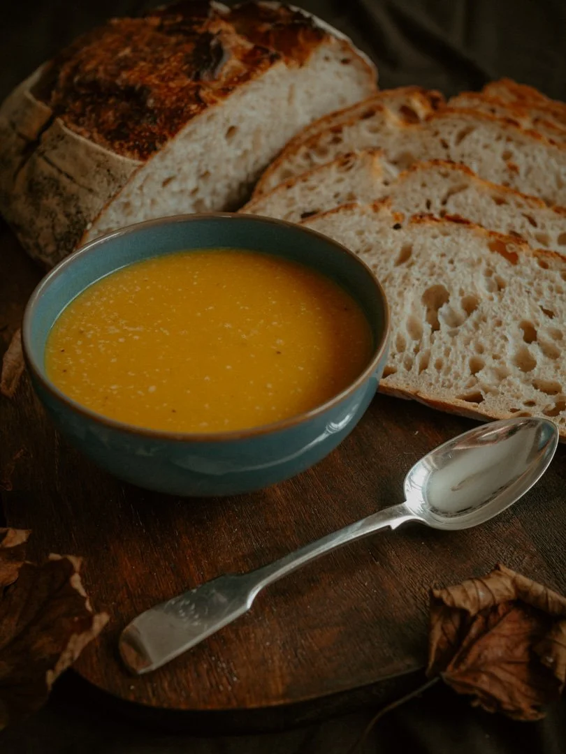 A bowl of warming spiced squash soup served with freshly baked sourdough bread in an autumnal setting.