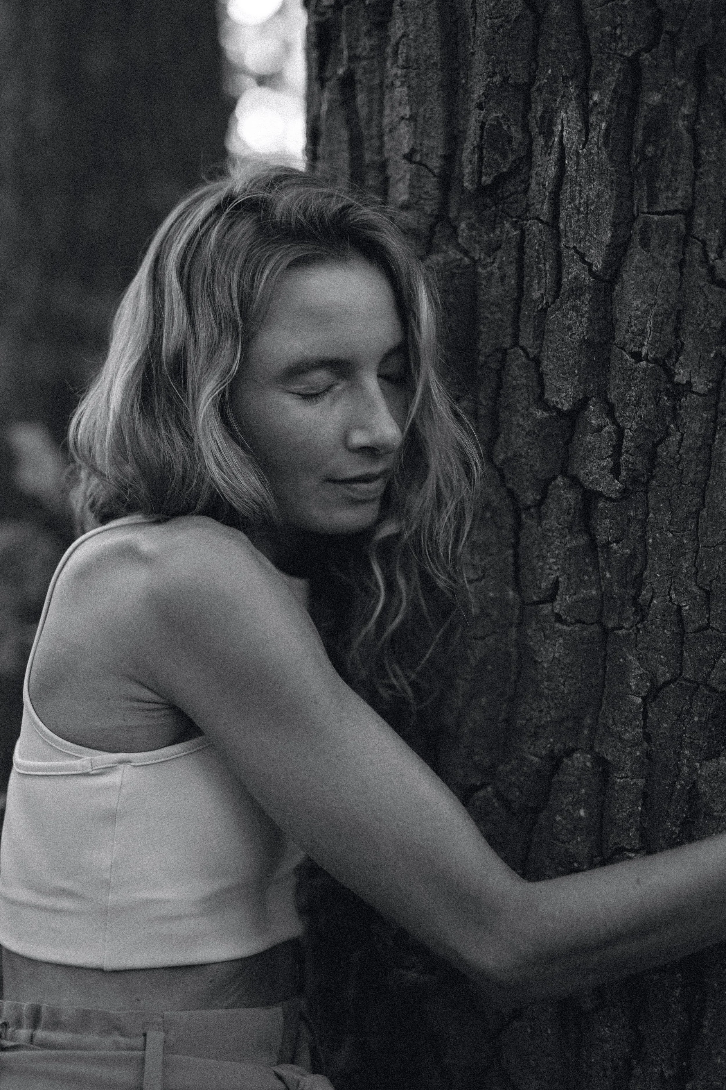 Verena Borell embracing a tree outdoors, reflecting grounding, healing, and connection with the natural world.