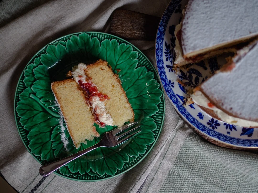 Slice of homemade Victoria sandwich cake with the full cake beside it.
