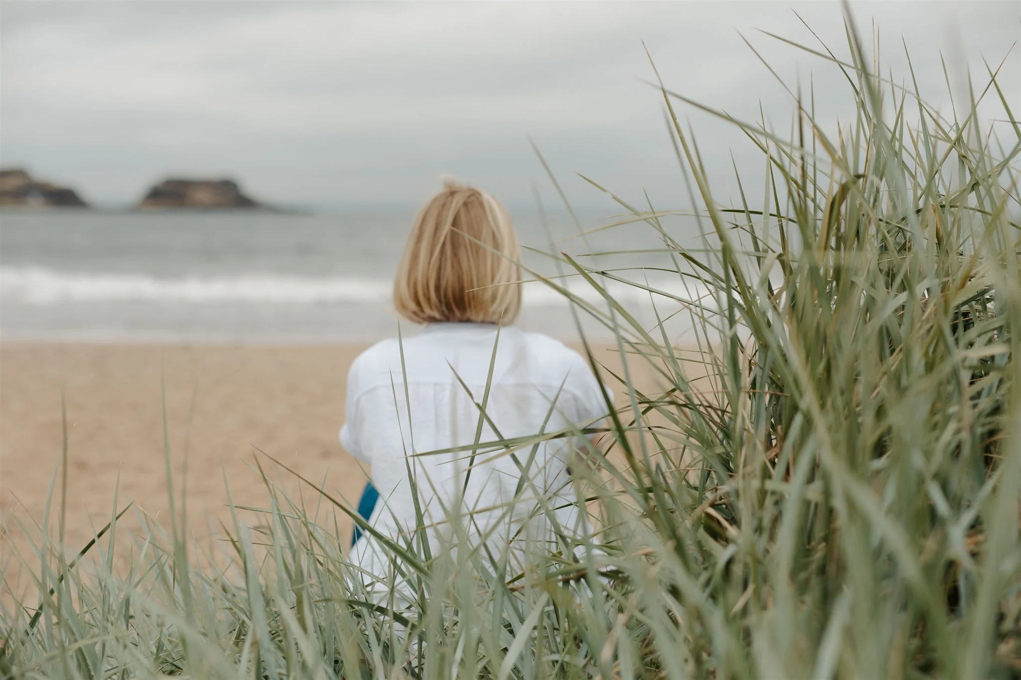 Sarah Philp sitting on the beach looking out to sea, embodying slow living, reflection and attentiveness to natural rhythms.