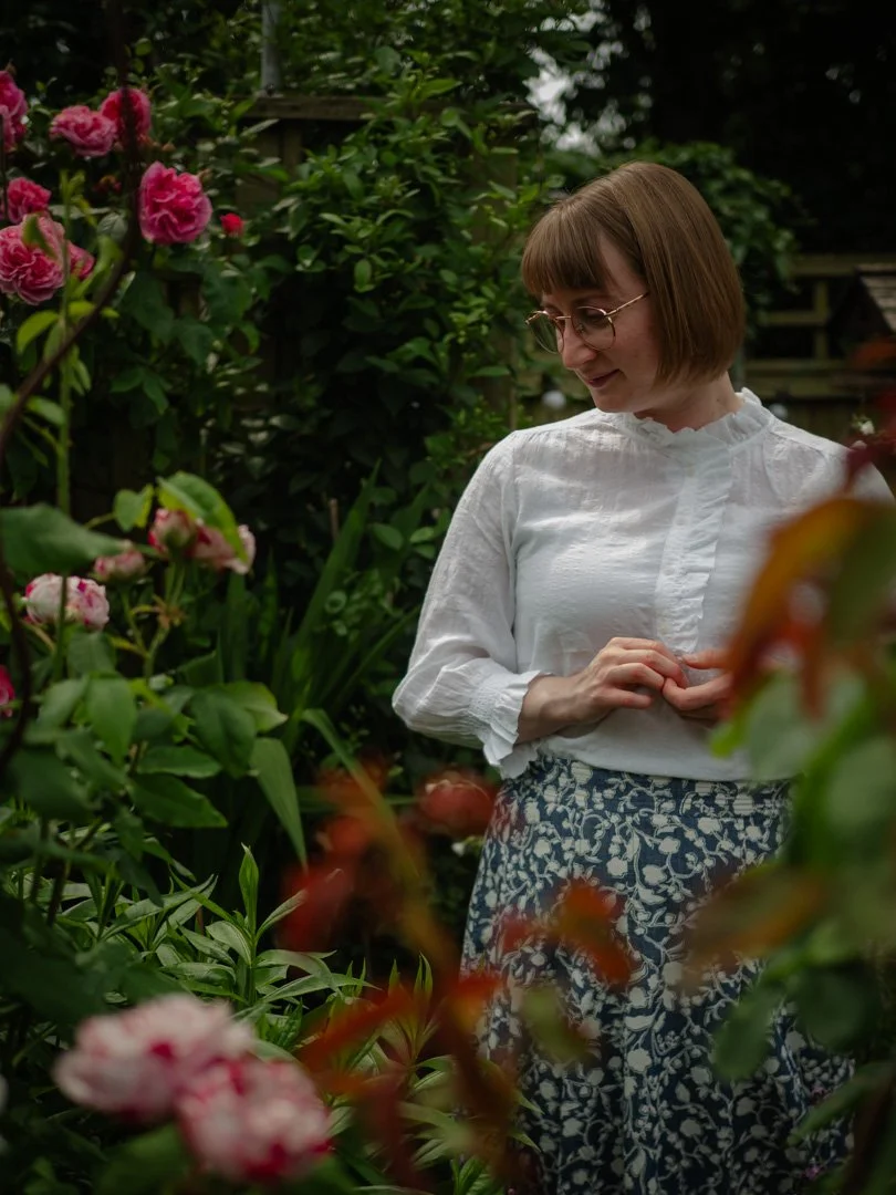 Clementine Rose standing thoughtfully in her garden among blooming roses
