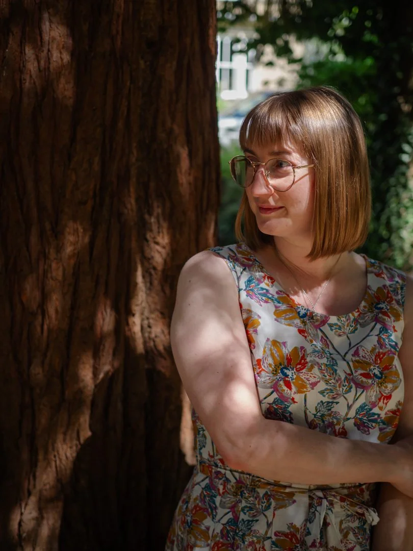 Clementine Rose standing beneath a tree in summer, surrounded by dappled light and nature