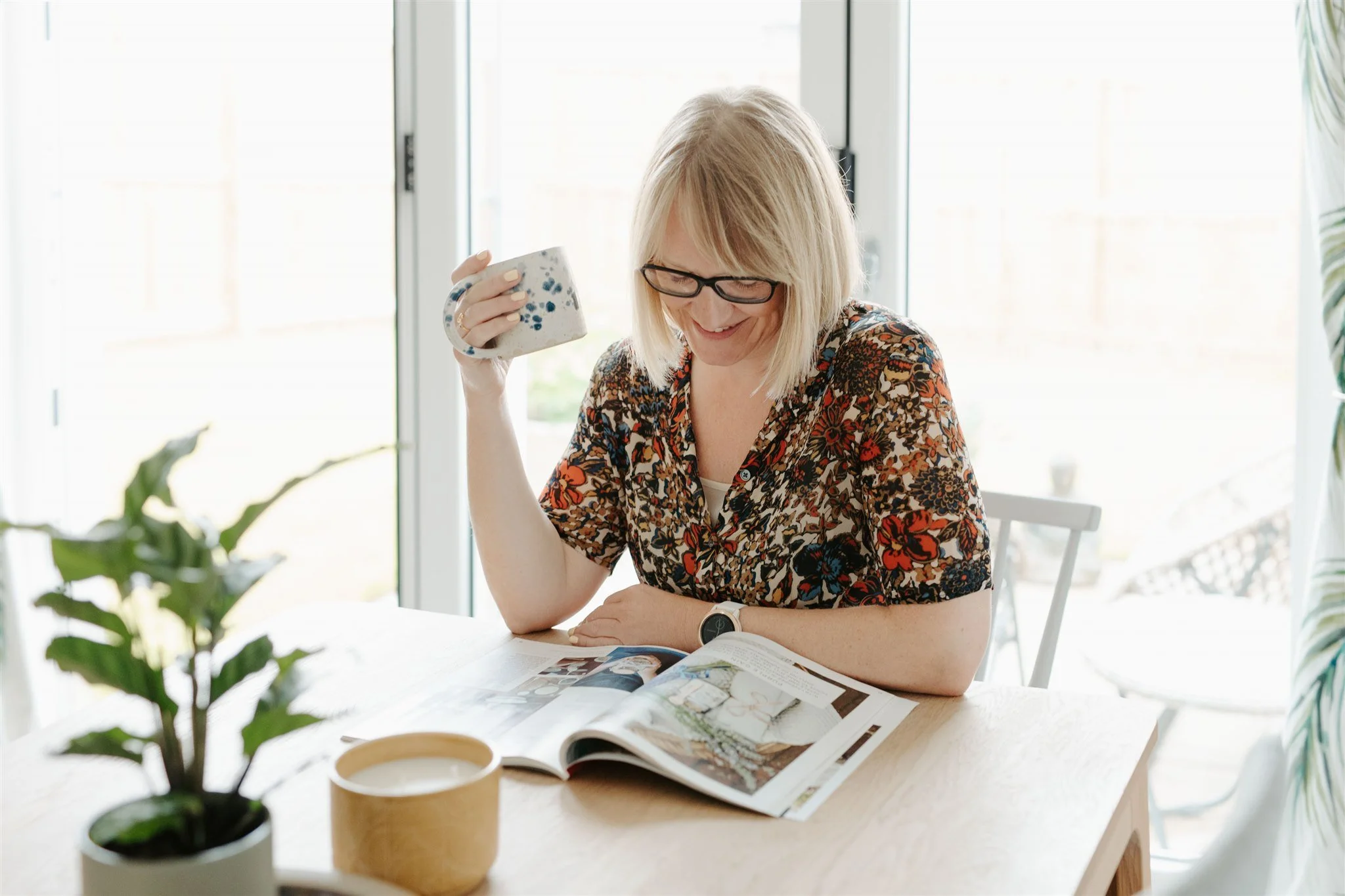 Sarah Philp sitting quietly at a table with a mug, reading and pausing in a moment of slow, mindful living.