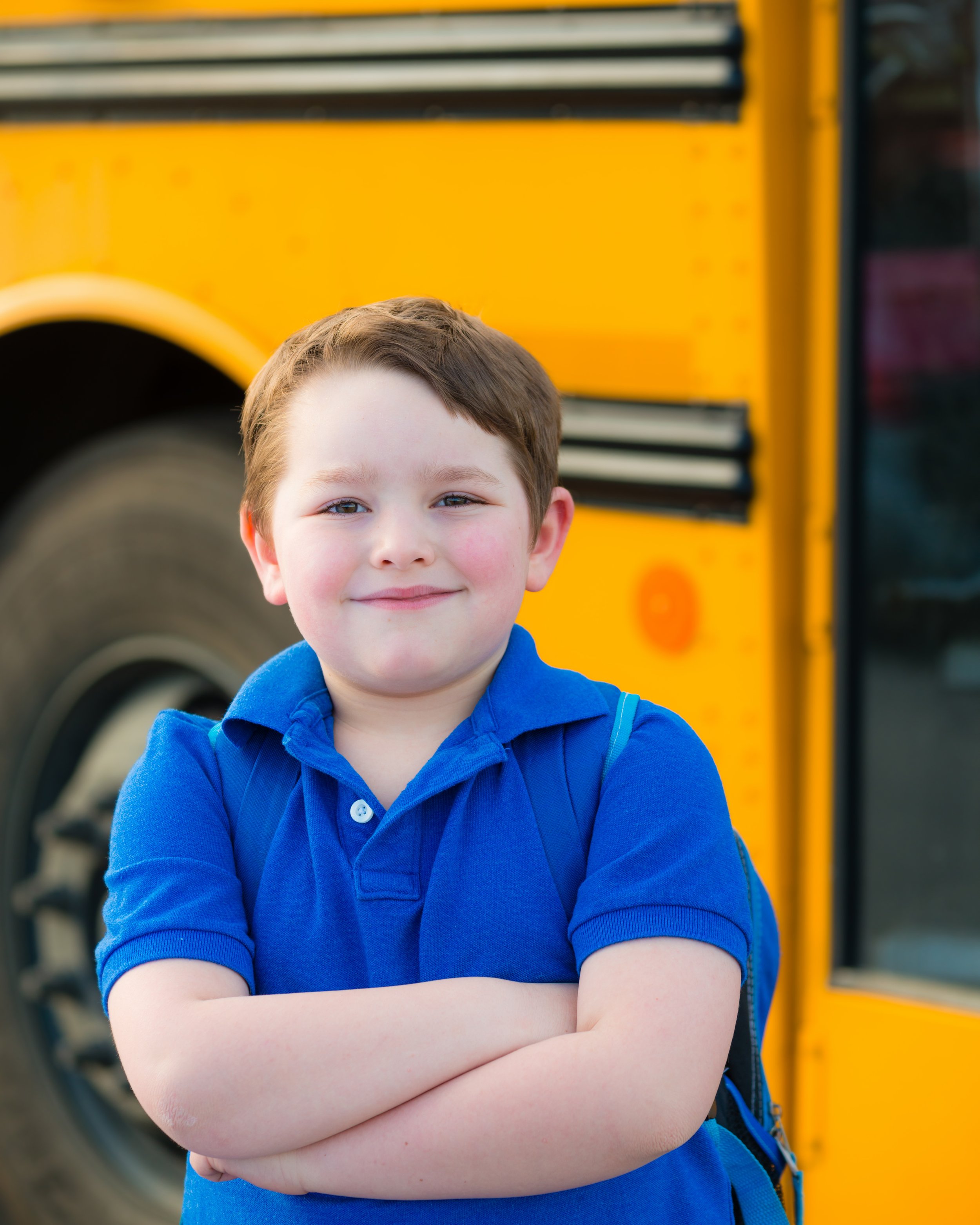 Elementary student of kindergartener in front of a yellow school bus showing customer's happiness with Haul Stars Charter Services
