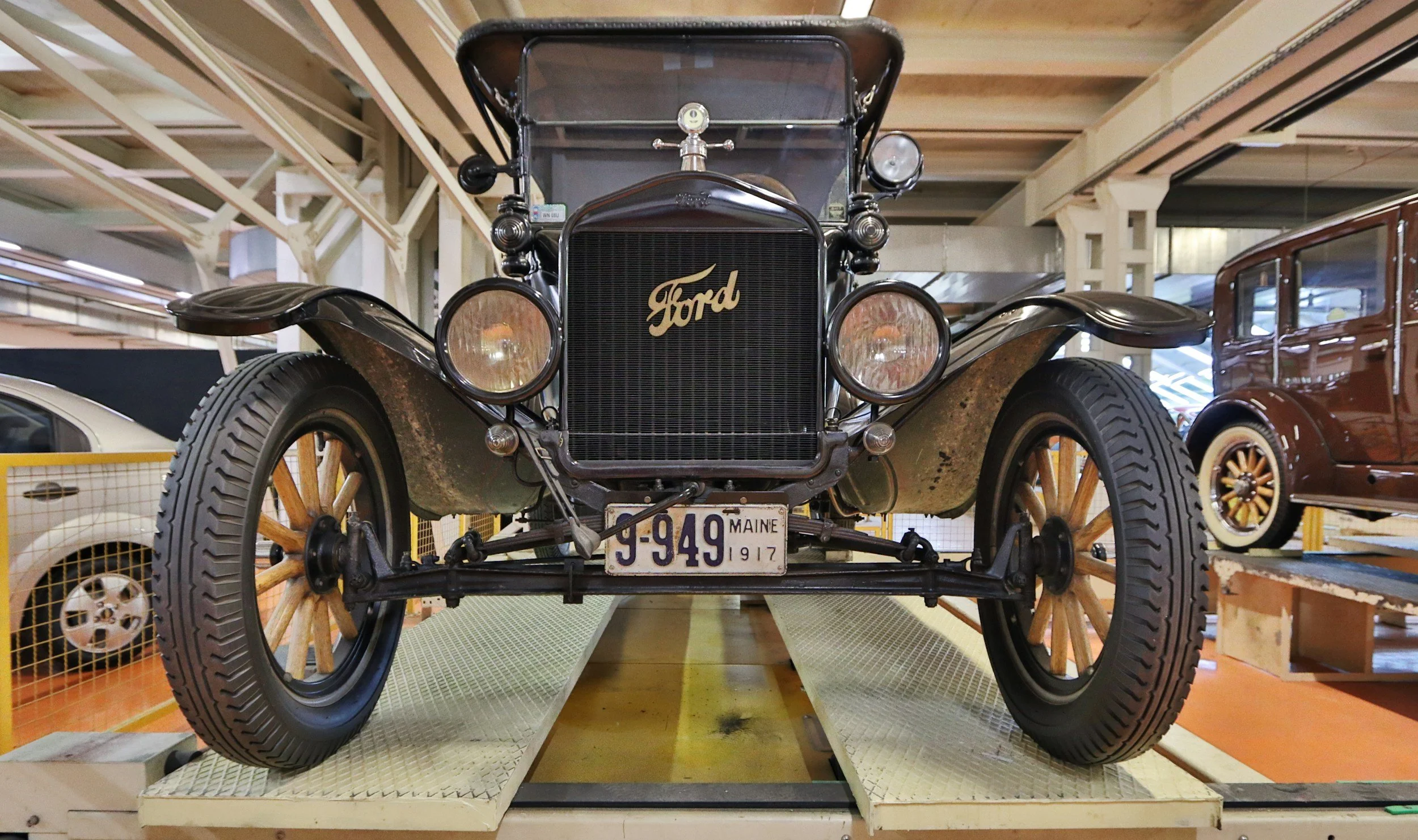 A vintage black Ford automobile from 1917 on display in a museum, with wooden spoked wheels, a brass radiator emblem, and an old license plate from Maine.