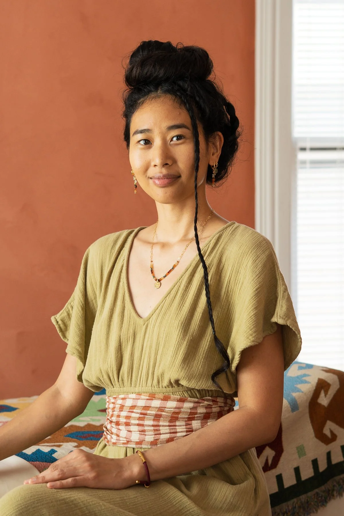 A portrait of Paulina Seng, Licensed Massage Therapist sitting next to her massage table in her wellness studio in the Houston Heights.