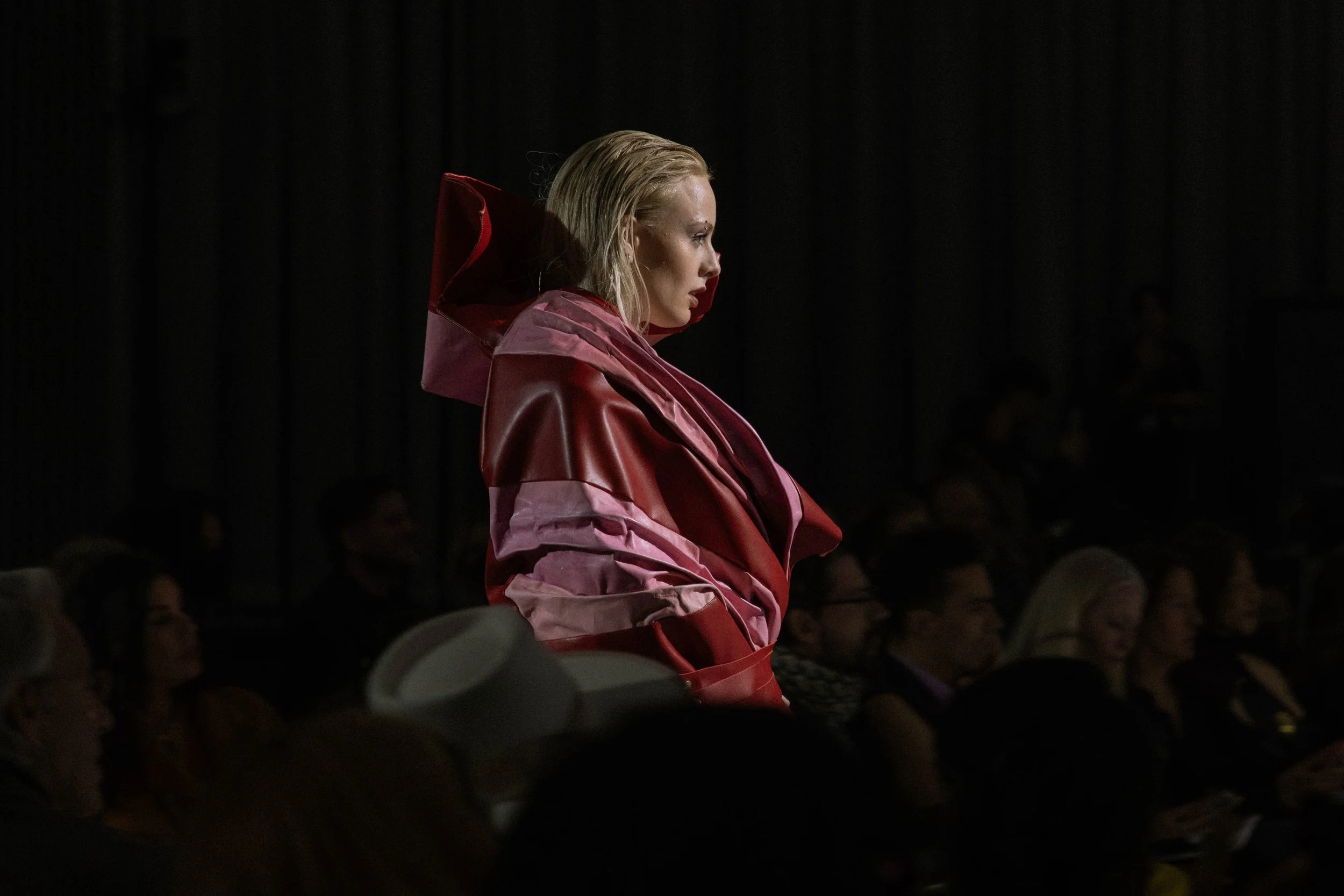 A model with light blonde hair wearing a multi-layer outfit in varying shades of pink on the runway at the GM Design Dome during the annual CCS Fashion Runway Show