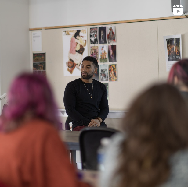 Mario Moore sitting on a desk at the front of an Illustration classroom at the College for Creative Studies