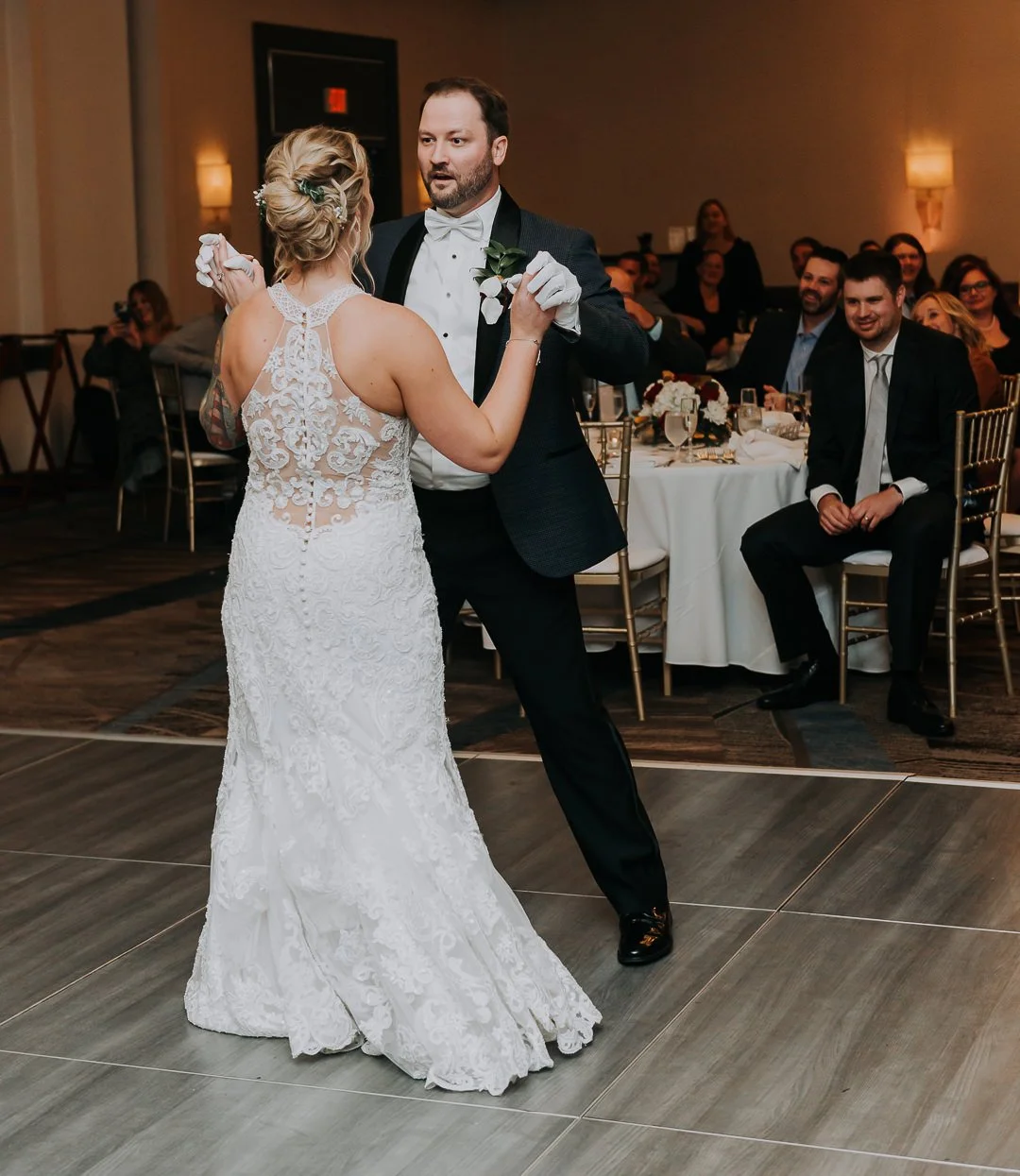 A bride and groom dancing at their wedding reception with seated guests watching and smiling in the background.