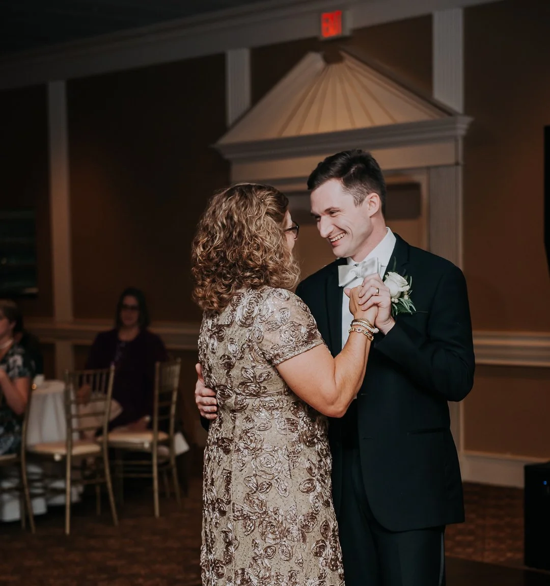 A bride and groom sharing a dance at their wedding reception, smiling at each other, with guests in the background.