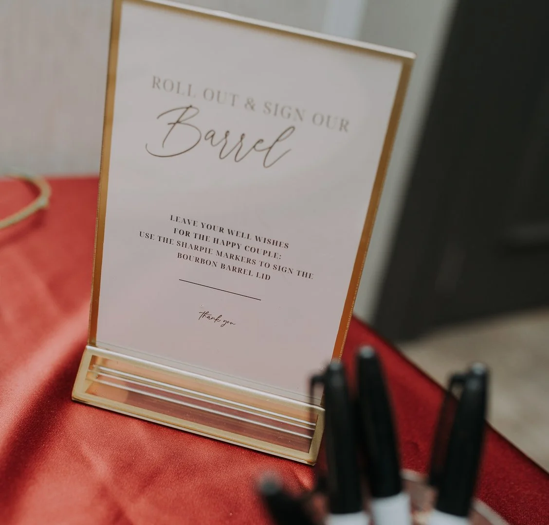 Sign with instructions for guests to sign a bourbon barrel lid using permanent markers at a wedding or event.