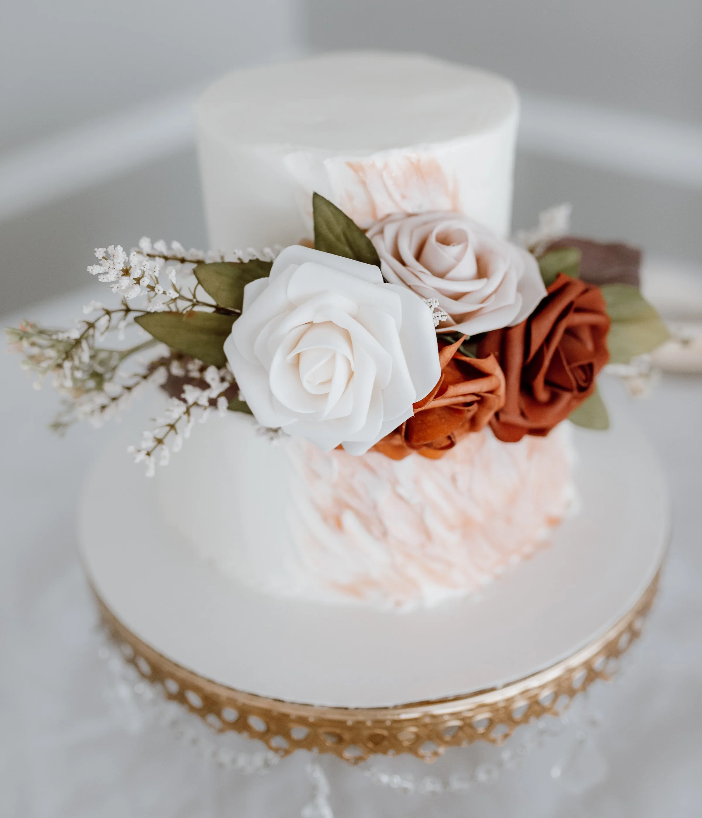 A small white cake decorated with white, pink, and brown flowers and green leaves on top.