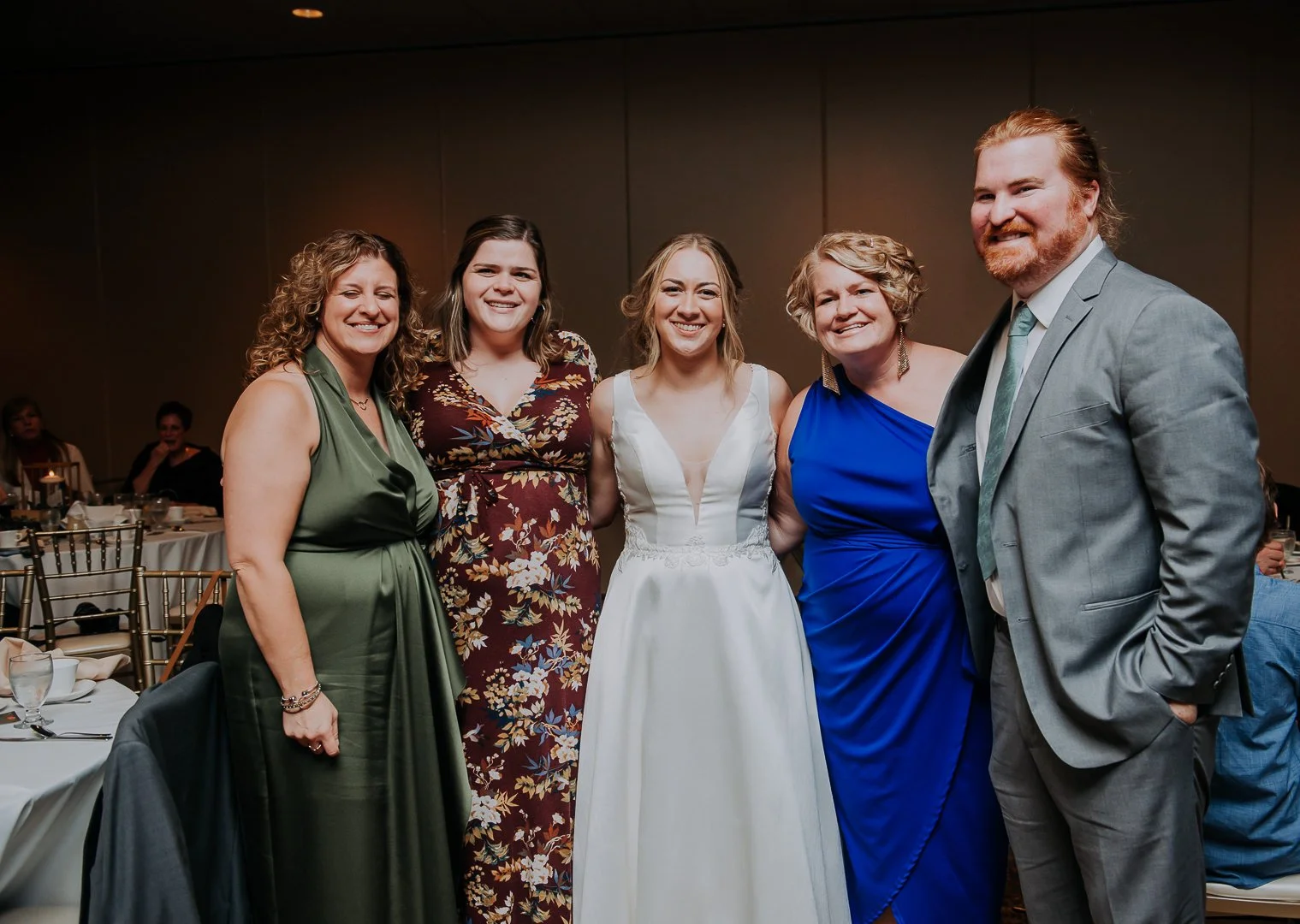 Group of five people smiling at a formal event, with women wearing dresses and a man in a suit.