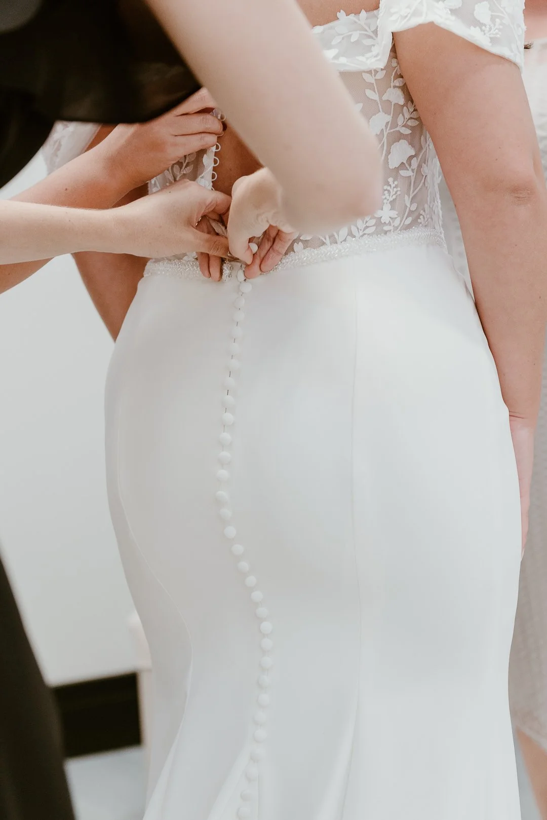Close-up of hands fastening buttons on the back of a bride's white wedding dress during dressing.