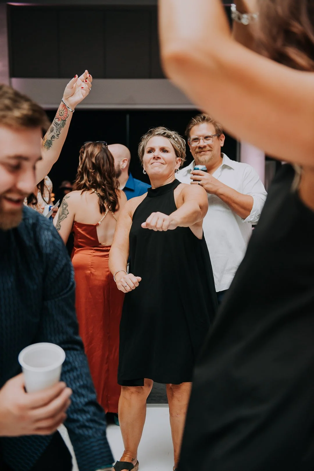 People dancing and socializing at a party or celebration, with a woman in a black dress confidently dancing in the center.