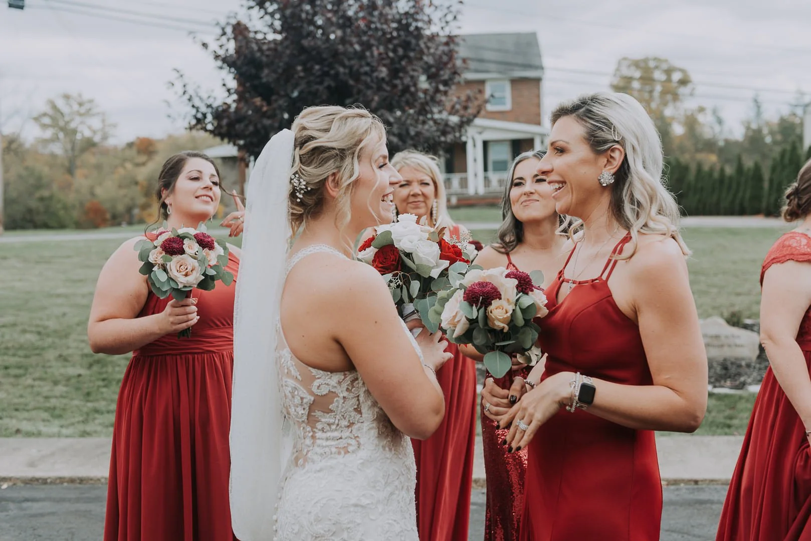 Bride and bridesmaids smiling and holding bouquets outdoors during a wedding.