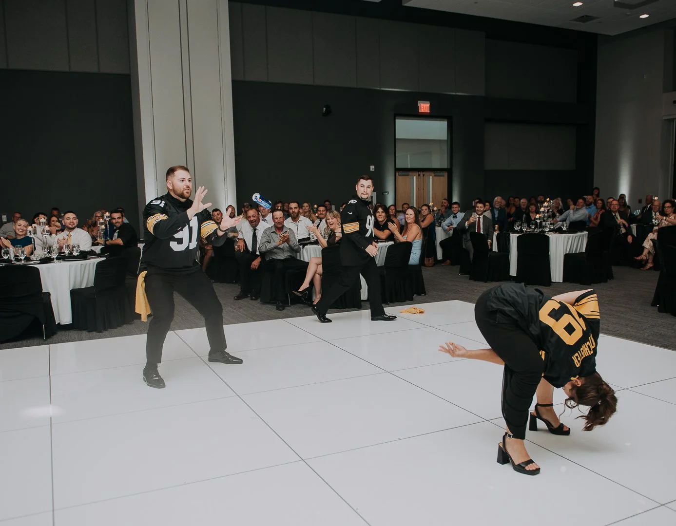 People at a banquet watching a dance performance by a woman in high heels and football jerseys on a white dance floor.