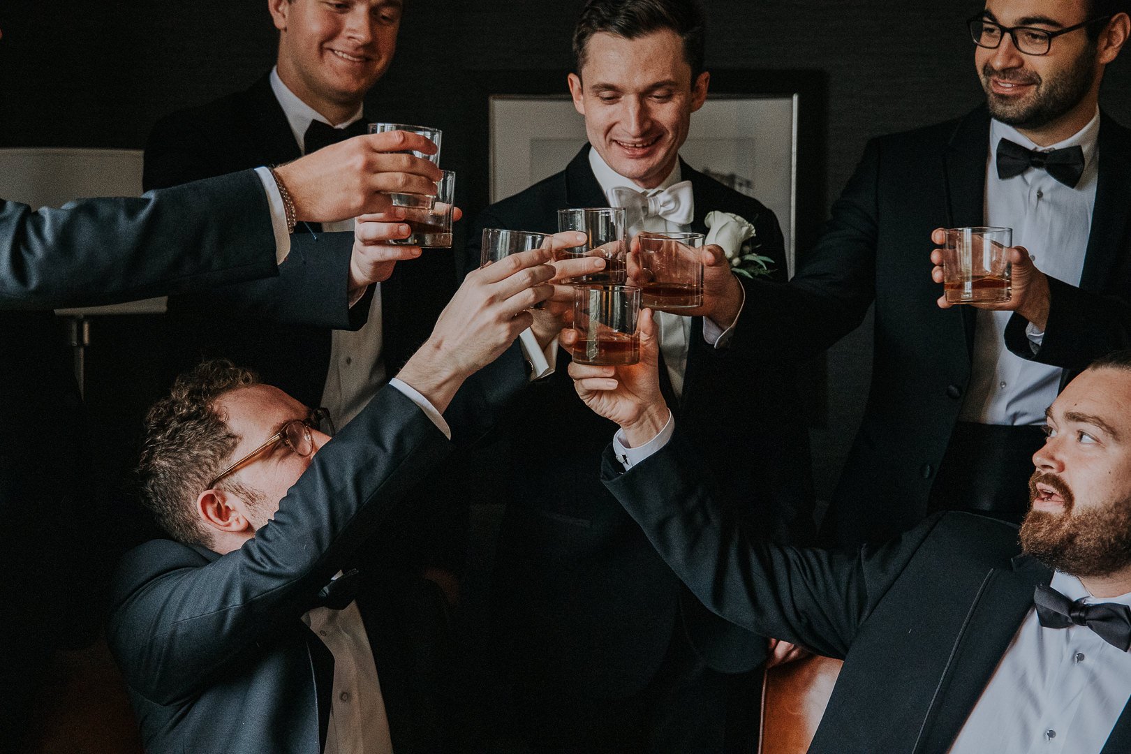 A group of men dressed in tuxedos celebrating with drinks in a toast at a formal event or wedding.
