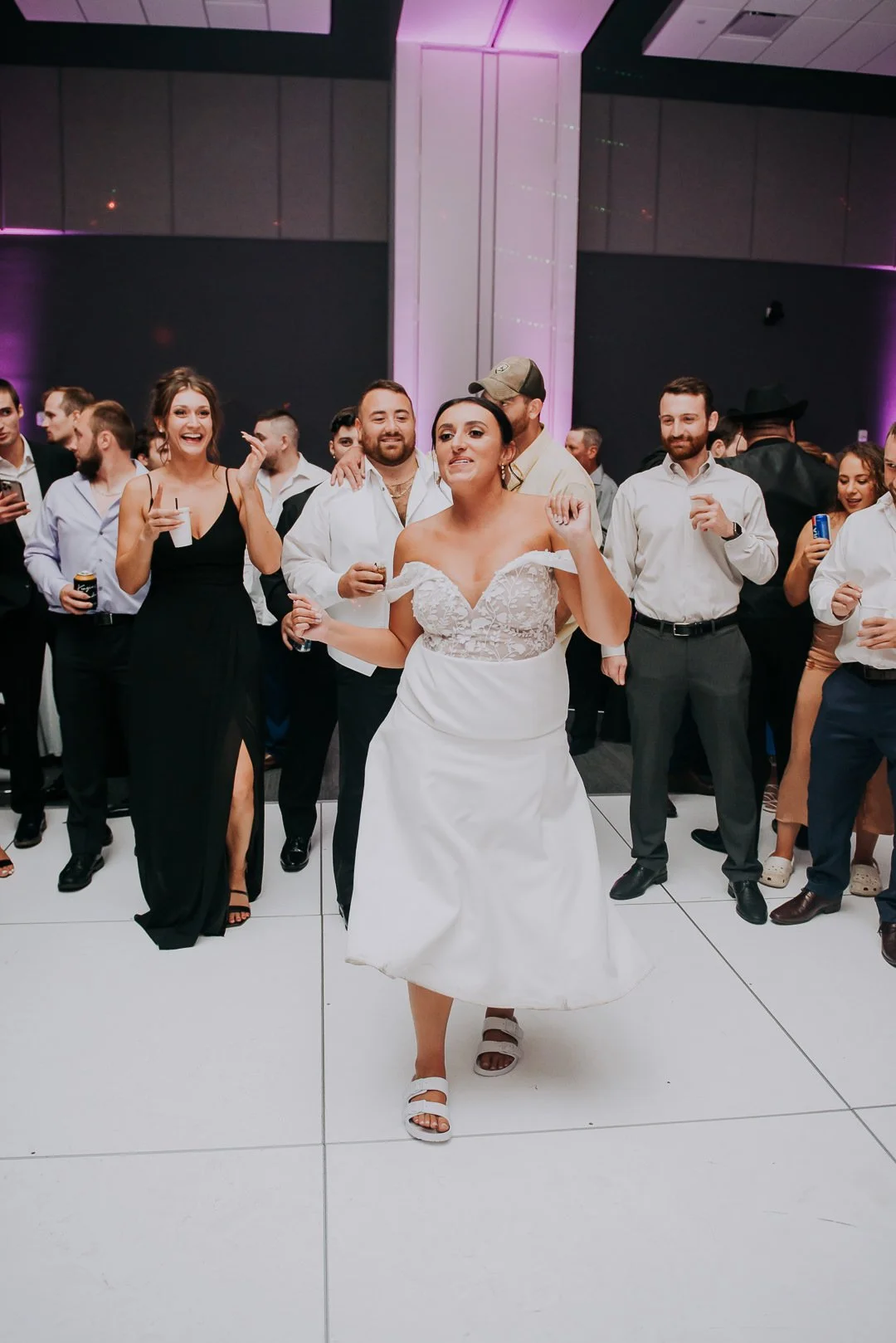 Bride dancing in a white dress at a celebration with guests in formal attire.